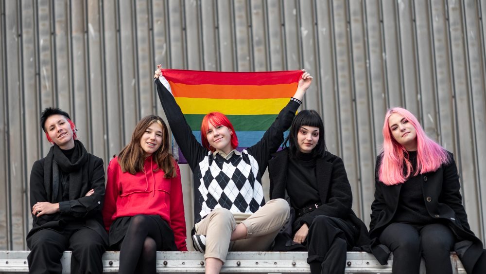 LGBTQ+ adults posing with a Pride flag