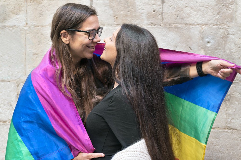 Two women sharing an affectionate moment beneath a Pride flag