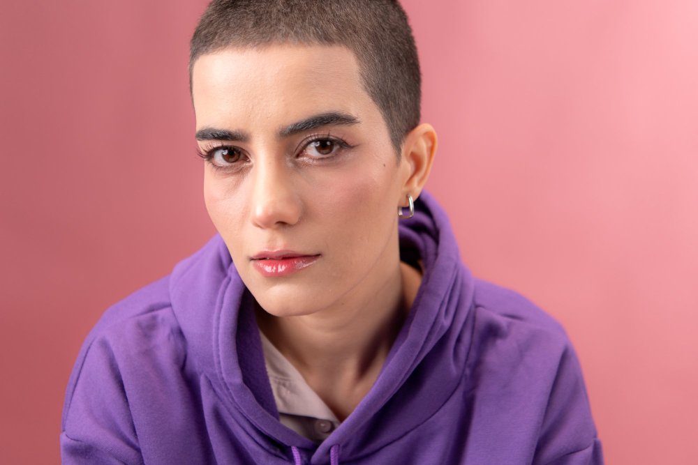 Transmasc person with short hair wearing a purple hoodie against a pink background