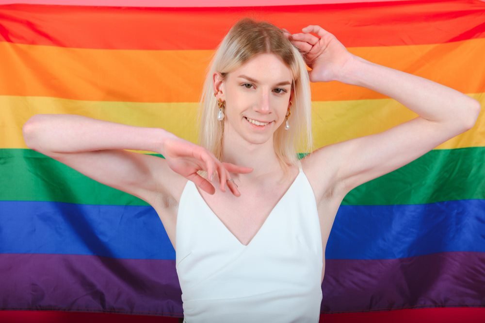 Smiling transgender woman in front of a Pride flag